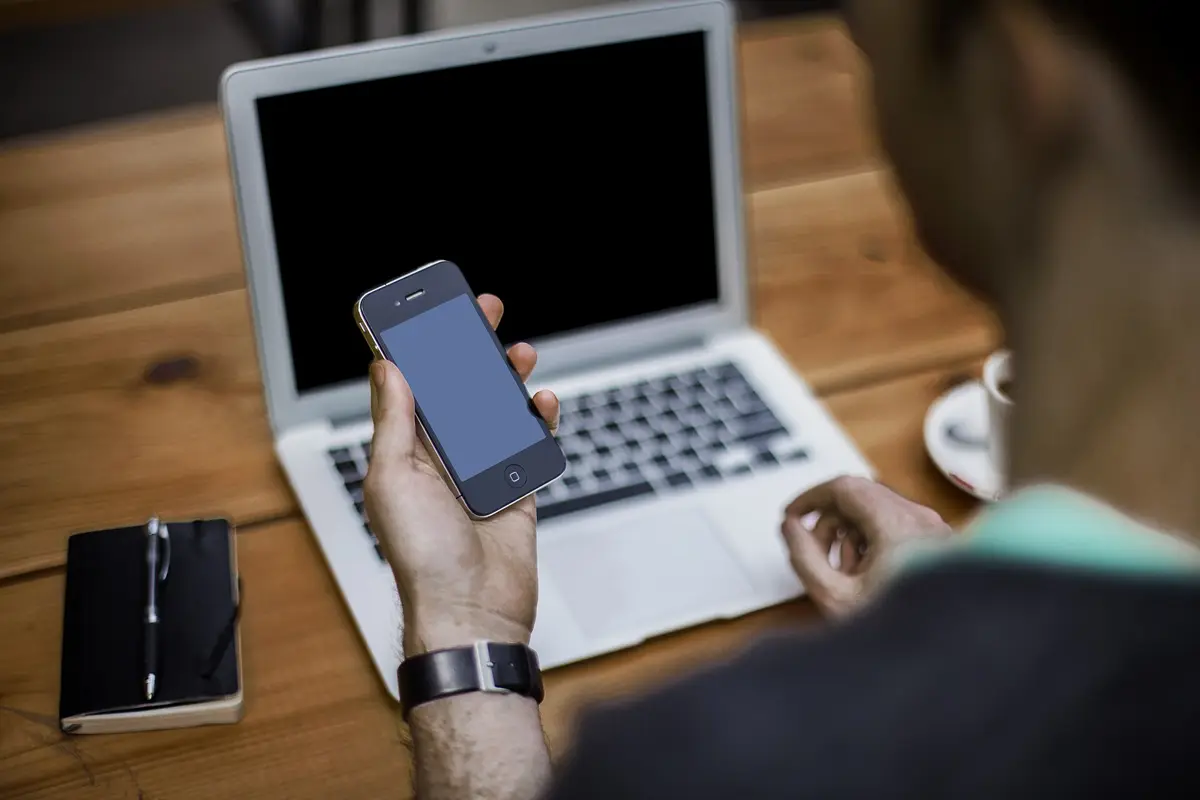 Person prüft ihr Smartphone vor einem Laptop